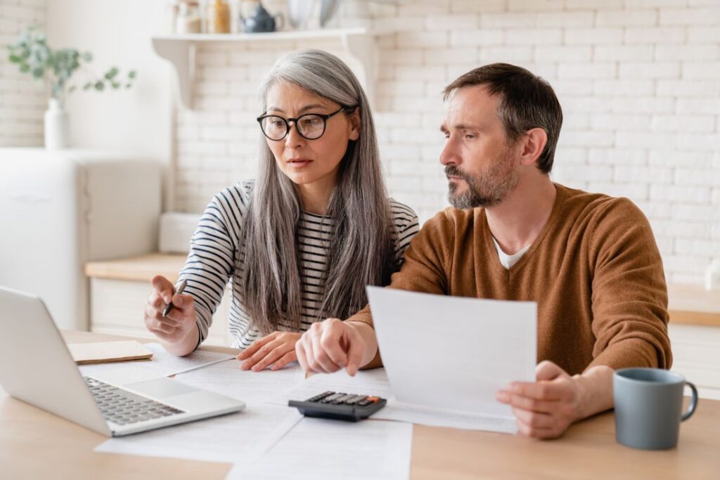 a couple sitting at a table and looking at a laptop to review their finances