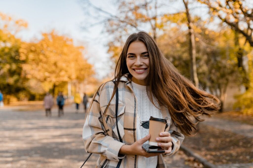 a woman smiling in a park while holding a cup of coffee
