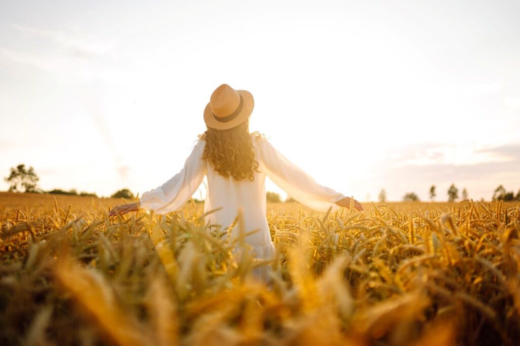 a woman standing amongst plants in a field during a sunset