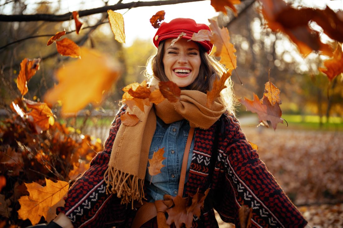a woman smiling amongst fall leaves in a park