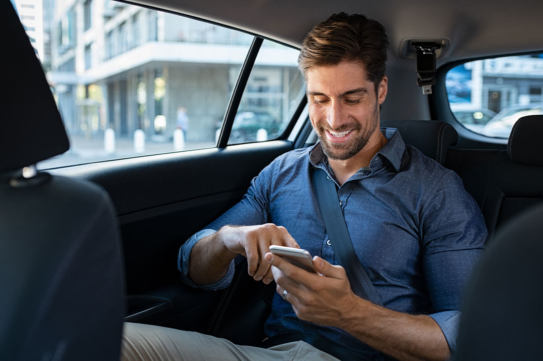 Happy smiling business man typing message on phone while sitting in a taxi.