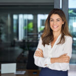 Confident business woman smiling standing in office arms crossed looking at camera