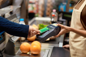 young adult man holding plastic credit card in hand, using terminal and paying for shopping in supermarket