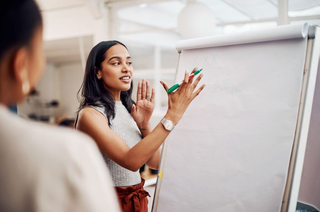 woman holding a marker near a whiteboard while speaking to a coworker