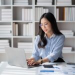 a woman sitting at a desk in an office and doing work on a laptop
