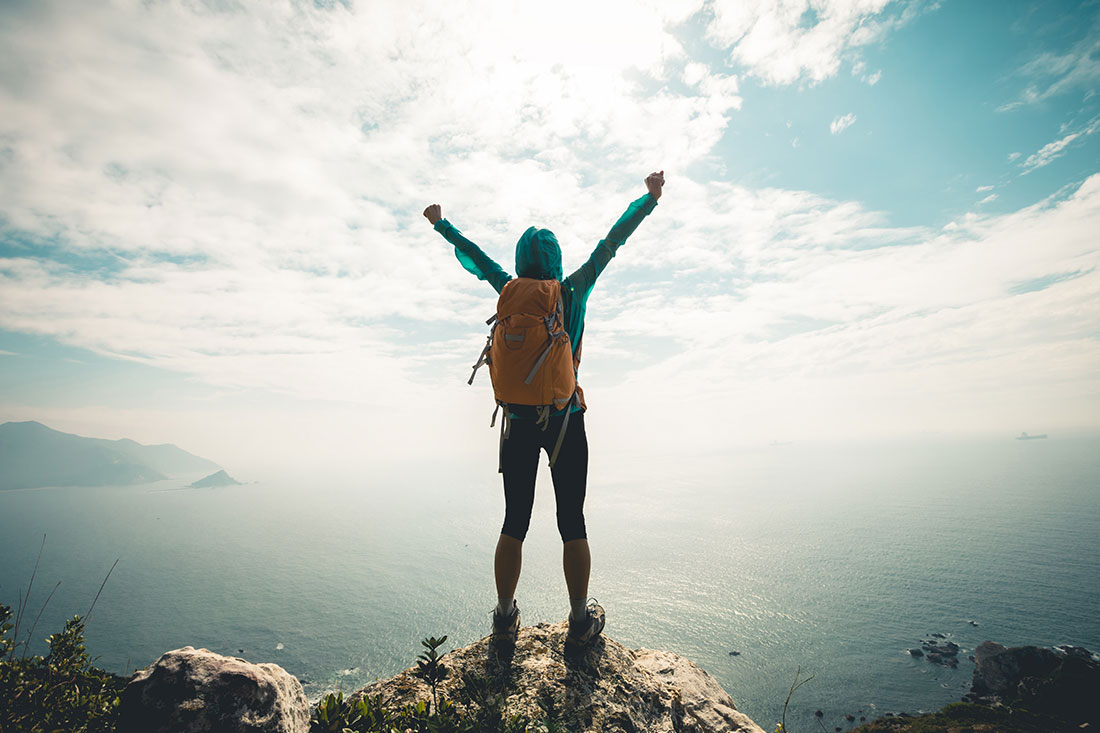 Successful hiker outstretched arms at seaside mountain top cliff edge