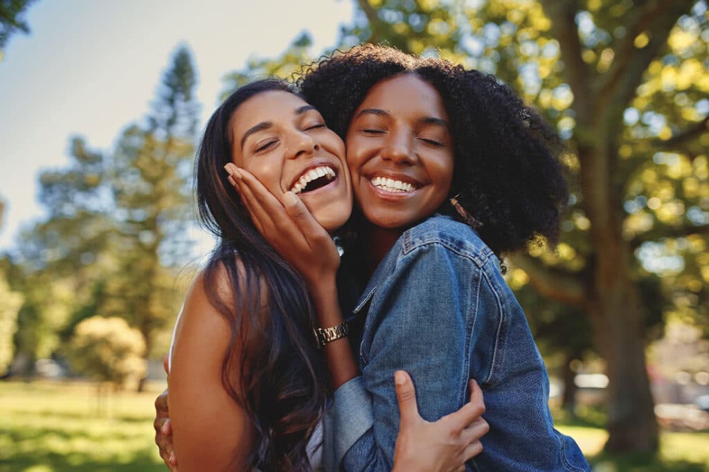 Close up lifestyle portrait of diverse multiracial happy best friends hugging each other and laughing in the park