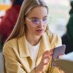 gen z woman using mobile phone looking at smartphone sitting at desk