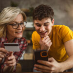 blonde woman and her teenager son shopping online use mobile phone and credit card