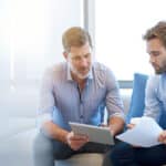 A sponsor using a digital tablet to discuss information with a younger colleague in a modern business lounge