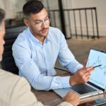 Financial advisor explaining invest stock market data consulting investor. Two busy business men analysts doing finance trading analysis pointing at exchange chart on laptop screen working in office.