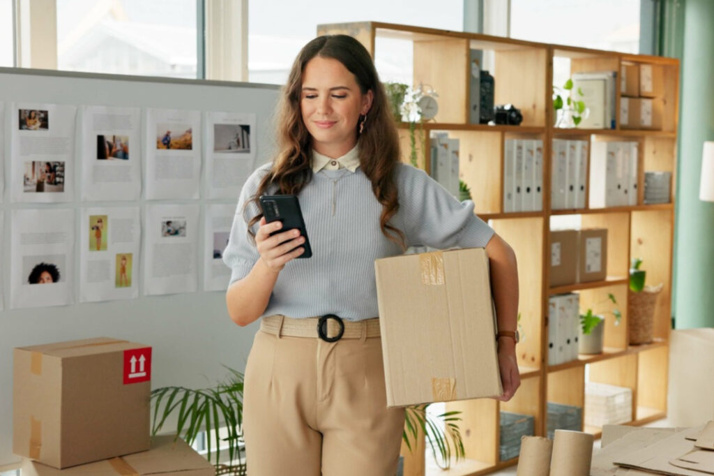 small business owner looking at her phone while holding a package