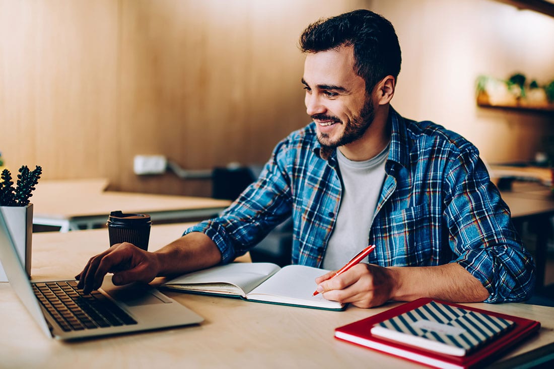 Man taking notes and working on laptop