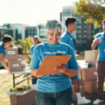 Happy, volunteers and mature woman with clipboard