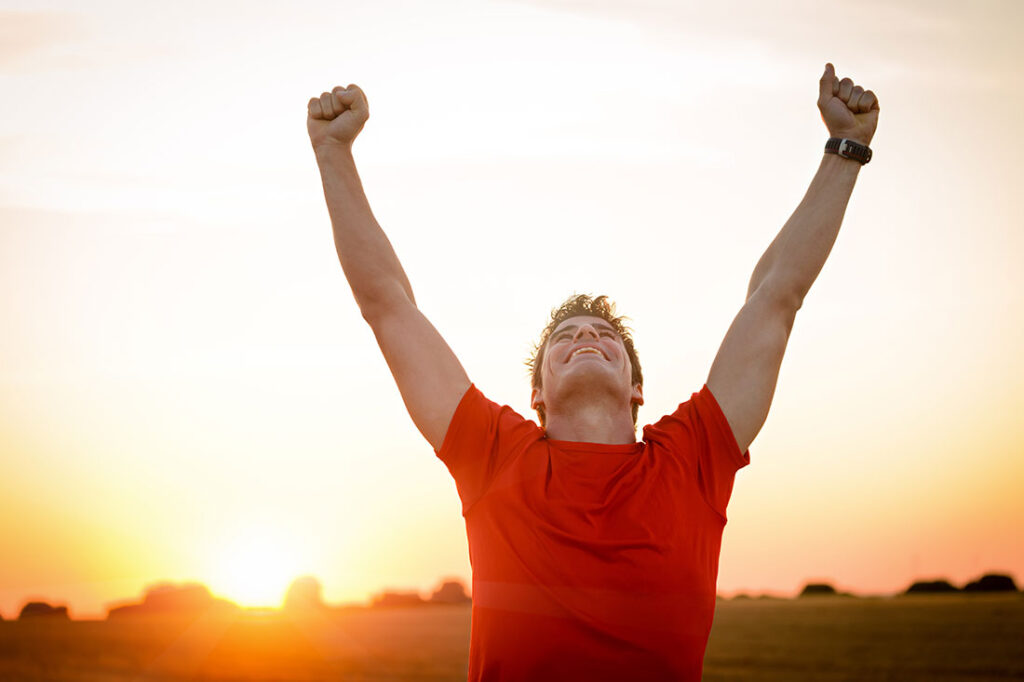Successful man raising arms after cross track running on summer sunset