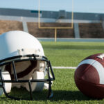 American football and helmet on field with goal post in background