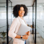 smiling woman holding her laptop where she uses productivity tools