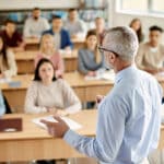 Back view of professor giving lecture to large group of students in the classroom