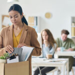 Upset businesswoman packing her things with coworkers in backdrop