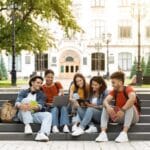 A group of students sitting on the steps of a college campus.