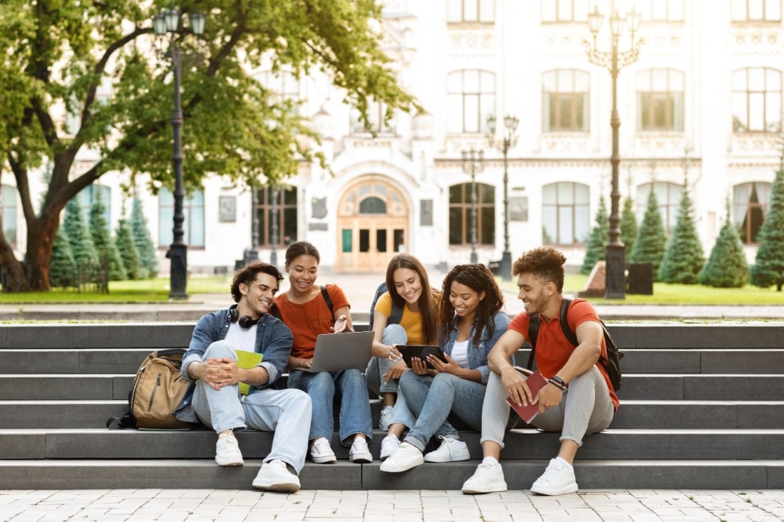 A group of students sitting on the steps of a college campus.