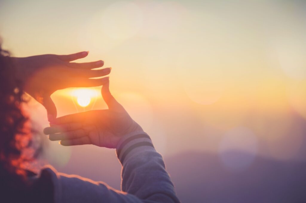 A woman makes a frame with her hands around the sun.