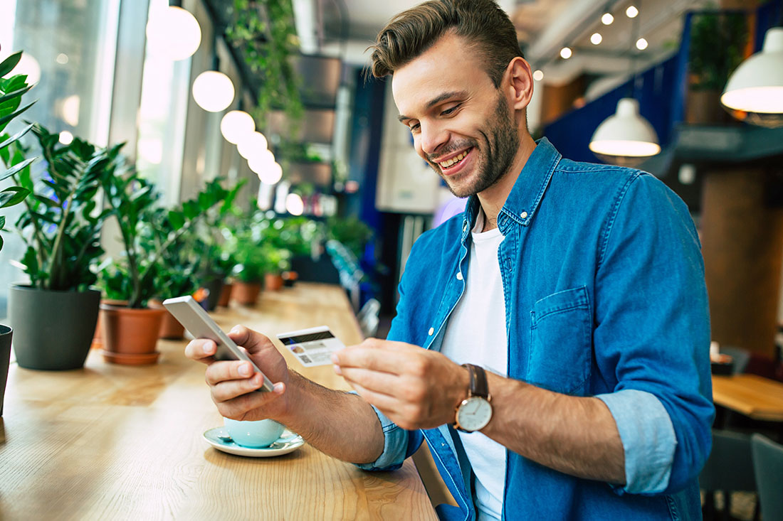young smiling man with credit card and phone in hands